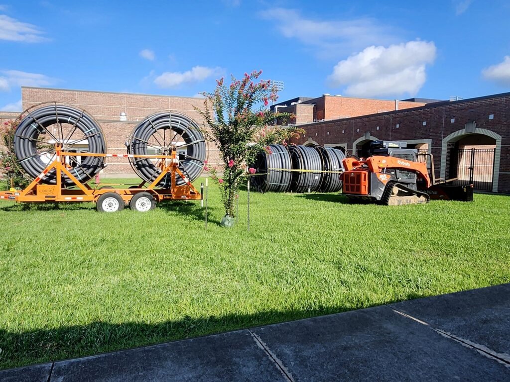 Underground utility installation setup with dual-reel HDPE conduit trailer, coiled conduit, and Kubota compact track loader.