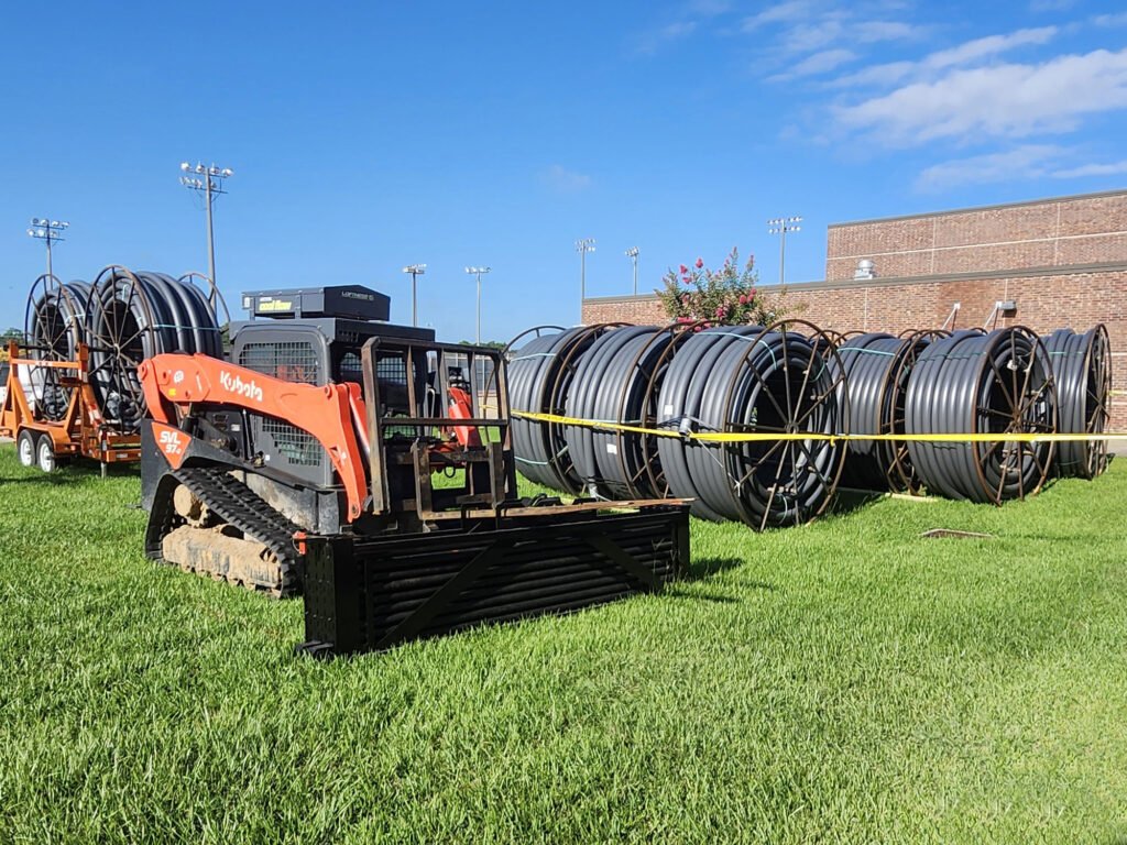 Kubota compact track loader beside reels of underground electrical conduit in a construction staging area